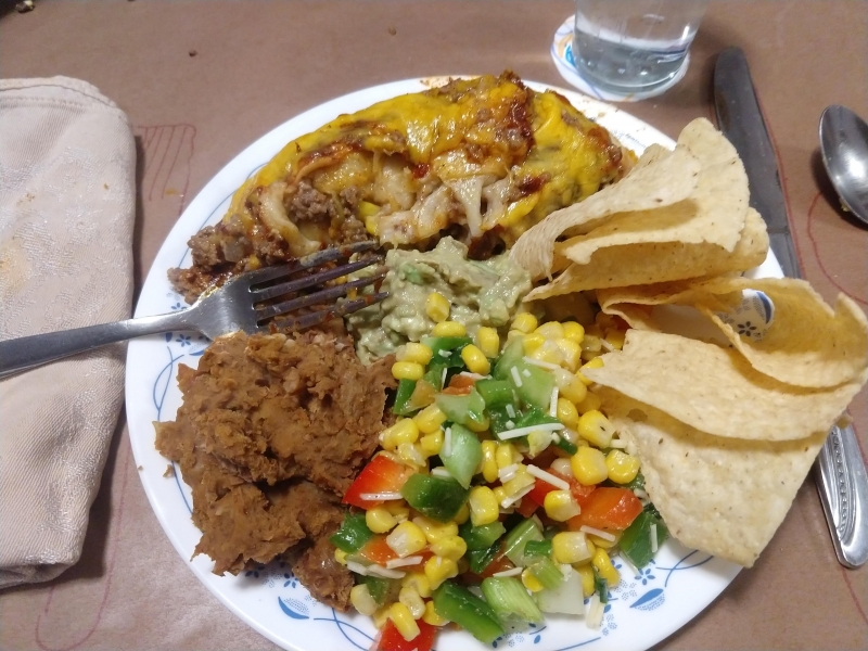 Beef enchiladas, corn chips with guac, corn salad, and refried beans